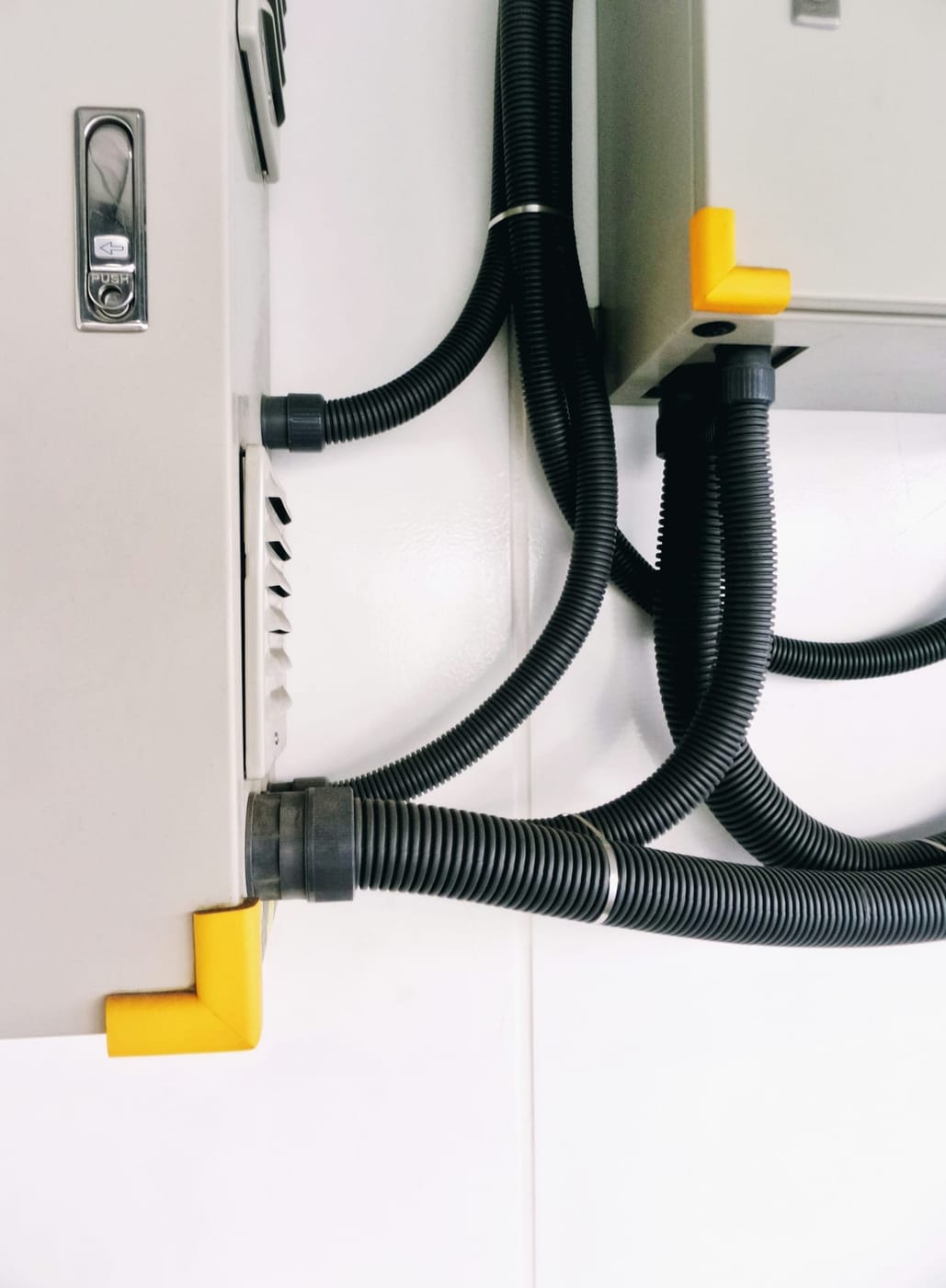 Vom Anlagenmechaniker angeschlossene flexible Leitungen an einem weißen Lüftungsgerät an der Wand