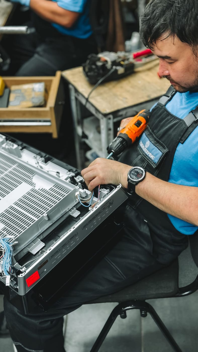Anlagenmechaniker öffnet ein Klima-Innengerät zur Wartung in der Werkstatt